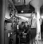 Sargeant Peter Degenstein of North Battleford, Sasketchewan (left) and Victor Isaac conducting final adjustments and tests on medium power transmitters prior to shipment at the RCA Victor plant juil. 1944