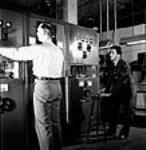 Sargeant Peter Degenstein of North Battleford, Sasketchewan (right) and Victor Isaac conducting final adjustments and tests on medium power transmitters prior to shipment at the RCA Victor plant juil. 1944