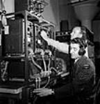 Sargeant Peter Degenstein of North Battleford, Sasketchewan (foreground) and Victor Isaac conducting final adjustments and tests on medium power transmitters prior to shipment at the RCA Victor plant juil. 1944