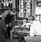 Sargeant Peter Degenstein of North Battleford, Sasketchewan (left) and Victor Isaac conducting final adjustments and tests on medium power transmitters prior to shipment at the RCA Victor plant juil. 1944