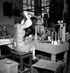 Woman worker overseeing spray-painting of Piat anti-tank gun bodies in a factory June 1944