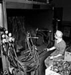 Woman worker overseeing spray-painting of Piat anti-tank gun bodies in a factory June 1944
