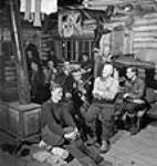 Lumbermen sitting around and enjoying violin music played by lumberman Romeo Clement of Farley, Quebec, in their bunk-house Mar. 1943