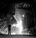 Workman supervises molten steel pouring from a ladle to an openhearth furnace at the Stelco Steel Company of Canada mars 1944