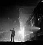 Workman supervises molten steel pouring from a ladle to an openhearth furnace at the Stelco Steel Company of Canada mars 1944
