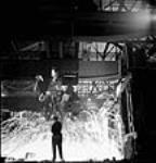 Workman observes ladles pouring molten steel at the Stelco Steel Company of Canada's openhearth furnaces mars 1944