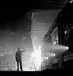 Workman supervises ladle pouring molten steel at the Stelco Steel Company of canada's openhearth furnaces mars 1944