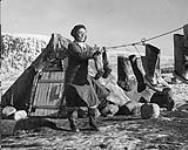 Une femme inuite met des bottes en peau de phoque à sécher devant sa tente à Pangnirtung. [Aasivak Evic, femme d'Angmarlik et grand-mère de la famille Evic, en train de faire sécher des " kamiks ". On aperçoit le Mont Duval en arrière-plan] n.d.