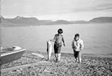 Jeune garçon [Daniel Qitsualik et Uimguk] Inuit [Inuuk] tenant une truite saumonée pêchée dans le détroit d'Éclipse, au large de l'île de Baffin October 1951