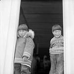 Two Inuit boys standing in a doorway. Cape Dorset August 1961.