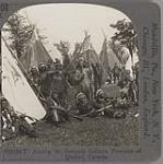 Iroquois in Native dress with rifles and traditional weapons standing among teepees 1890-1910