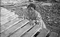 Inuit girl beside dock. [Maryann Tattuinee. This photograph was probably taken at Coral Harbour, Southampton Island. Ms. Tattuinee now lives in Rankin Inlet.] ca. 1945-1946 [ca. 1945-1946].