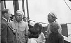 Inuit with Rev. A.C. Herbert aboard R.M.S. Nascopie at Pond Inlet (Mittimatalik/Tununiq), Nunavut, August 1945 [Joseph Idlout is the man in the hat standing on the left and Simon Anaviapik is the man wearing a hat standing on the right] August 30-31, 1945.