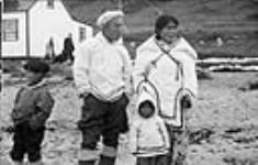 Inuit family [Ipeelie (Ipilee) Merkosak and his wife Leah Sigluk Merkosak with their son Akittiq on the left, and daughter Martha (Mata) in the middle] standing outside at Pond Inlet (Mittimatalik/Tununiq), Nunavut, August 1945 August 30-31, 1945.