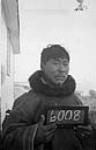 Man [David Arnatsiaq] holding a small chalk board with the number 6008 at Pond Inlet (Mittimatalik/Tununiq), Nunavut, August 1945 30-31 August 1945.