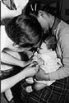 Nurse is injecting a needle into a baby's arm at Frobisher Bay General Hospital 1959