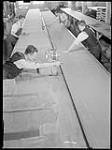 Workmen operate a power cutting machine to cut through many thicknesses of cloth for army service uniforms at the Great Western Garment Co 16 Apr. 1942