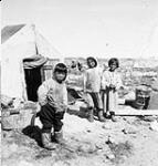 Three Inuit children standing in front of their summer tent [graphic material] 1951 ?