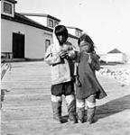 Two unidentified Inuit girls standing in front of a Hudson's Bay Company outlet [graphic material] 1951 ?