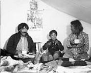 Chesterfield Inlet (Igluligaarjuk) Inuit family drink tea while young boy samples raw salmon trout 1946 or 1947.