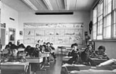 Sir Joseph Bernier Federal Day School (Turquetil Hall), group of students working at their desks in a classroom, Chesterfield Inlet (Igluligaarjuk), Nunavut, September 5, 1958. [1st row: Rene Otak is on far left; 2nd row: Pete Irniq is on the far right, beside him is Paul Manitok; 3rd row: Nick Anautinuq is on the far right; 4th row: Raymond Kalak is seated second from the left.] [graphic material] : September 5, 1958.