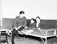 Constable V.H. March-Bank on a cot with two Inuit girls in the U.S. Airforce Hospital 1944