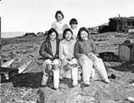 Inuit children seated on a wooden crate beside a qamutiik (sled) 1949