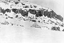 Group of Inuit standing outside by tupiit (skin tents), Kugaryuak River, Coronation Gulf, Northwest Territories [Nunavut] May, 1916