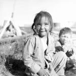 [Des enfants, Marion Tupiq et Peter Kukkiak, sont assis sur le sol à l'extérieur, Baker Lake (Qamanittuaq), Nunavut] [entre juin-septembre 1963].