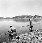 Two Inuit men putting a kayak into the water 1948