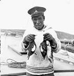 Inuk man holding two pitsulaks (birds) he shot 1949
