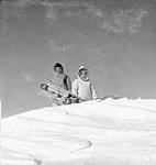 Two Inuit boys on top of a snow bank with a sled 1950