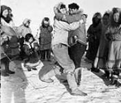 Inuit men wrestling surrounded by a group of women and children 1950