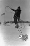 First Arctic WInter Games. Inuit games; ipirourtaqturniq whip contest. A silouetted player shows his power by using a 30ft whip to flick closely-spaced objects, such as tin cans, off a snow bank Mar. 1970.