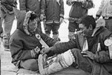Two Inuit men compete in a game of aqsaaraq or tug-of-war during the ceremonies of the First Arctic Winter Games. Yellowknife, N.W.T., March 1970. [The men have been identified as Guy Amarok (left) and Jack Anguk Sr. (right).] March 1970.