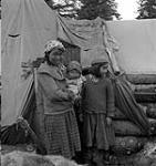Inuit girl and woman holding a baby outside of their tent on the Strutton Islands of James Bay January, 1946.