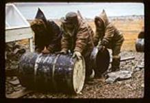 Men rolling oil barrels on the ground, Cape Dorset, Nunavut [between August 24-October 3, 1960]