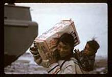 Woman carrying a child in her amaut and a large bag of sugar over her shoulder [between June 17-October 31, 1960]