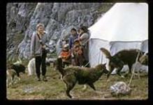 Group of people [Lizzie Unatweenuk, Martha Unatweenuk, Sammy Unatweenuk, Peanina Assivak] and huskies standing outside of a tent, Killiniq, Nunavut [between July 24-August 9, 1960]