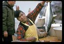 Inuit man [Johnny Makalu (Morgan)] holding up Arctic char, Kangiqsualujjuaq (George River), Quebec [between July 16-August 9, 1960]