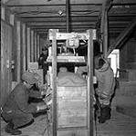 [Men operating a fur press, Kinngait, Nunavut] [between 1956-1960]