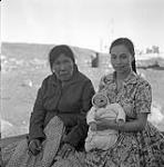 [Two women [left to right: Ooa, Inga Alainga] sitting with a baby [Maleektoo Alainga] outside, Iqaluit, Nunavut] [between 1956-1960]