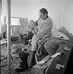 [Mackenzie Porter removing his boots inside a tent] [between 1956-1960]