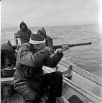 [Mackenzie Porter aiming a gun from a boat with three bystanders] [between 1956-1960]