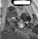 [Mosha Michael (right) teaching Barbara Hinds (left) how to make a polar bear stew, near Iqaluit, Nunavut] [between 1956-1960]