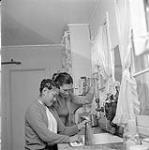 [Two young women [woman on left is Elisappe Avinga] cleaning a fish in the kitchen, Iqaluit, Nunavut] [between 1956-1960]
