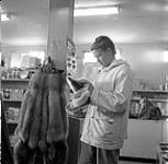 [Barbara Hinds looking at fur moccasins inside of a store] [between 1956-1960]