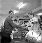 [Barbara Hinds (right) and a cashier exchange money in a store] [between 1956-1960]