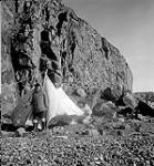[Mosha Michael standing in front of a tent being pitched by Pitseolak, near Iqaluit, Nunavut] 1960