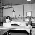 [Two women folding sheets at a laundry facility, Iqaluit, Nunavut] 1960
